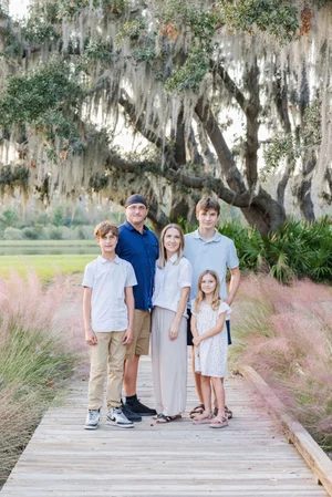 Family portrait on wooden path with trees and pink grass background