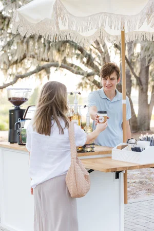 A person at an outdoor coffee stand receiving a drink from the barista.